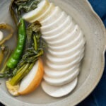 Dongchimi served in clear chilled brine with sliced Korean radish and greens