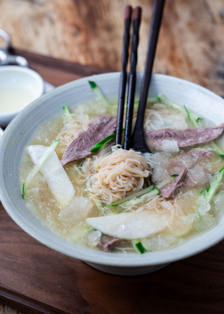 mul naengmyeon korean cold noodle soup with chopsticks lifting noodles in icy broth