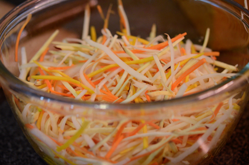 Sliced root vegetables are combined in a mixing bowl.