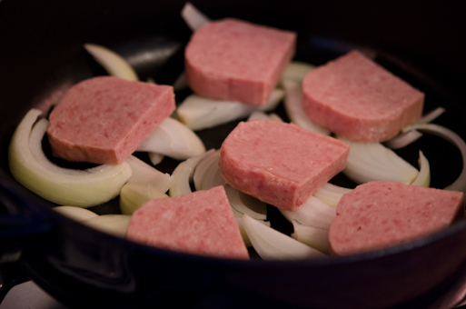 Spam slices are placed on the onion slices in a pot.
