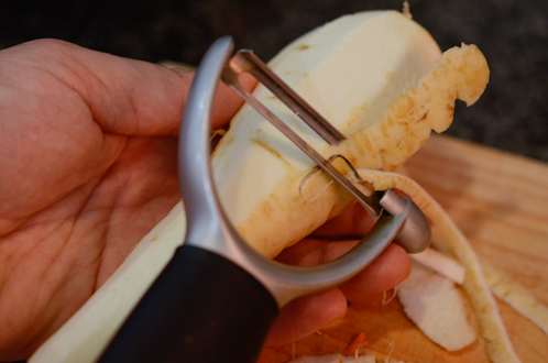 A vegetable peeler is peeling the skin of a parsnip.