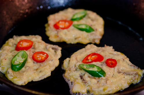 2 slices of fresh red and green chilies are placed on top of Bindaetteok batter in a skillet.