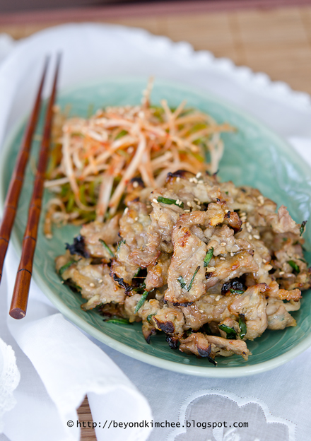 Doenjang marinated Korean pork is broiled and served with green onion salad on a plate.