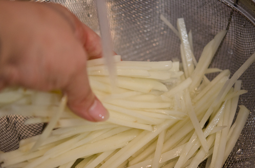 Potato matchstick slices are being rinsed under the running water.