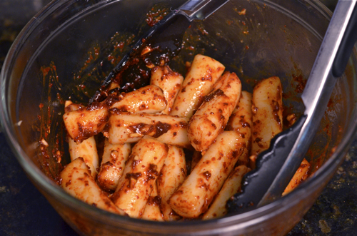 Rice cakes are tossed with spicy sauce in a bowl.