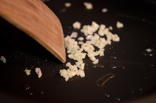 Chopped garlic is in oil with a wooden spatula in a skillet.