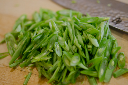 A green bean is cunt into thin French cut diagonal slices.