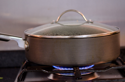 A skillet covered with a lid is on the medium flame over the stove.