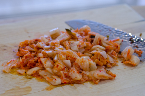 Cabbage kimchi is chopped into small pieces with a knife on the cutting board.