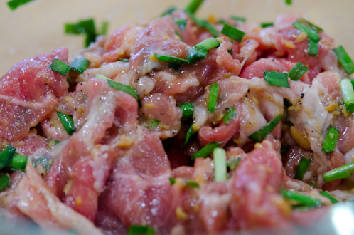 Thin pork slices are added to doenjang marinade and tossed together in a bowl.