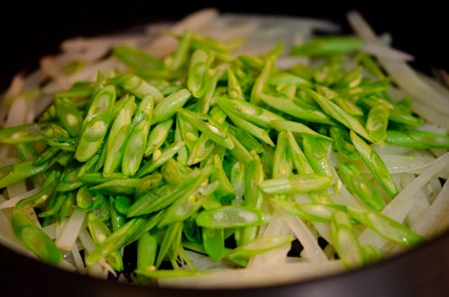 French cut sliced green beans are added to potato slices in a skillet.