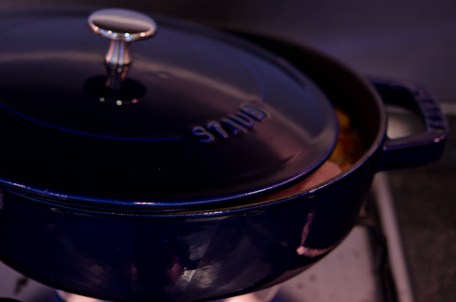 A pot of kimchi stew is covered with a lid but slightly open on the side and placed over a stove.