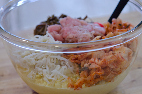 Ground pork, mung bean sprouts, kimchi, and fernbrakes are combined in a large bowl.
