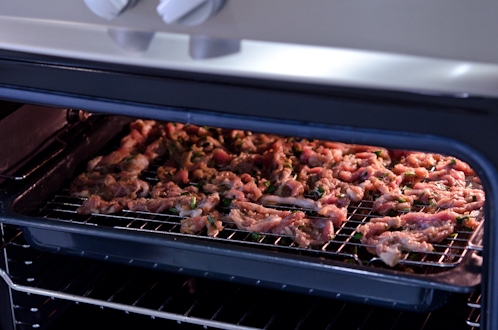 A rack of Korean marinated pork is entering under a broiler to cook.