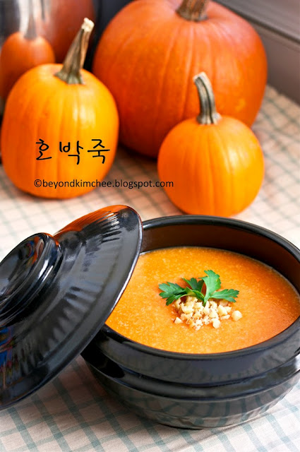 Korean Pumpkin Porridge is served in a stone pot surrounded by pumpkins.